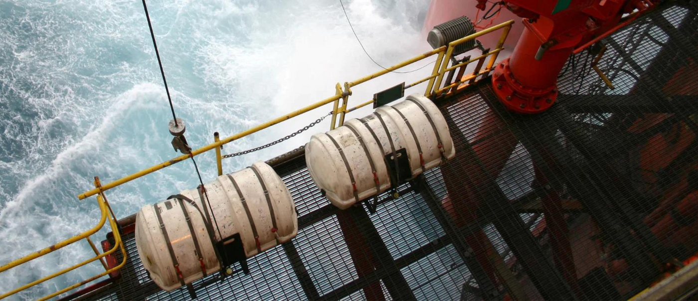 life rafts in round container on metal cat walk with water in the background.